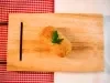 Fotografia vista de cima de um croquete frito de carne moída sobre uma tábua de madeira. Tem um pequeno ramo de salsinha decorando o croquete.