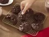 Fotografia de uma grelha quadriculada ao lado de um copo de vidro com leite e nescau. Sobre a grelha tem sete cookies de nescau extra cacau com gotas de chocolate e um mão feminina pegando um. Fotografia de uma grelha quadriculada ao lado de um copo de vidro com leite e nescau. Sobre a grelha tem sete cookies de nescau extra cacau com gotas de chocolate e um mão feminina pegando um.