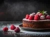 Fotografia de um bolo de chocolate rico, decorado com framboesas vermelhas e mirtilos, polvilhado com açúcar de confeiteiro. Folhas de hortelã adicionam frescor.