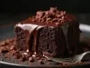 Fotografia de um pedaço de bolo de chocolate em um prato escuro. O bolo é rico e úmido, coberto com ganache brilhante e decorado com pedaços de chocolate.