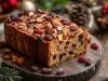 Fotografia de um bolo de frutas natalino, adornado com uma camada brilhante e coberto com nozes e frutas secas, rodeado por elementos festivos como pinhas e enfeites, evocando um clima aconchegante de celebração.