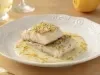 Filés de bacalhau servidos com molho cremoso de ervas e raspas de limão, apresentados em prato branco elegante.