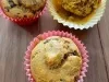 Fotografia de três forminhas de cupcake com bolo de cenoura e uva passa, sendo duas de tom rosa e uma amarela. Os cupcakes estão sobre uma mesa de madeira.