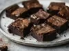 Fotografia de um prato raso de tom cinza claro sobre uma mesa cinza. Dentro do prato tem oito pedaços de brownie.