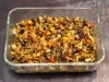 Em cima de uma mesa, refratário com berinjelas, pimentões e cebolas picados, regados com azeite.