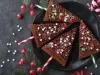 Em cima de uma mesa, prato redondo preto com brownie em forma de triângulo, decorado com ganache e confeitos de bolinhas e estrelas coloridos.