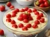 Imagem de um recipiente de vidro com um creme branco e decorado com morangos inteiros.