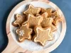 Em cima de uma mesa, prato com biscoitos em formato de estrelas, decorado com glacê branco.