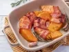 Em cima de uma mesa, há um refratário quadrado com abóboras cortadas em meia-lua enroladas com bacon.