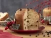 Imagem de um panetone caseiro com gotas de chocolate cortado em um prato vermelho, com decorações de Natal.