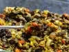 Em cima de uma mesa, colher com berinjelas, pimentões e cebolas picados, regados com azeite.