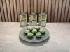 Prato cinza com docinhos verdes cobertos por granulado branco, acompanhado de latas de Leite Moça ao fundo.