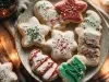 Em cima de uma mesa, prato redondo com biscoitos de estrela, árvore de Natal, decorados com glacê colorido e confeitos coloridos.