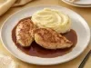 Pedaços de frango dourados servidos com purê cremoso de batata e molho escuro reduzido, apresentados em prato branco elegante