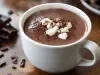 Imagem de uma xícara branca com chocolate quente com pedaços de marshmallow branco.