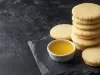 Em cima de uma mesa, biscoitos amanteigados dourados e redondos crocantes.