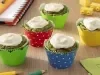 Fotografia de cinco muffins de espinafre, cada um dentro de forminhas coloridas. Sobre cada um tem um creme caseiro com ninho, e estão sobre uma mesa de madeira.