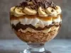 Em cima de uma mesa, refratário com biscoitos crocantes, doce de leite, bananas em rodelas, decorado com chantilly, bananas em rodelas e raspas de chocolate.