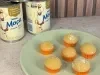 Docinhos claros cobertos com açúcar em forminhas laranja, servidos em prato verde com Leite Moça ao fundo.