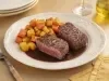 Dois bifes altos ao ponto servidos com molho reduzido escuro e raízes assadas douradas, apresentados em prato branco elegante