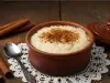 Em cima de uma mesa, tigela com arroz doce cremoso, com uma textura suave e aveludada, decorado com canela em pó.