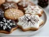 Em cima de uma mesa, prato redondo com biscoitos de estrelas, decorado com glacê branco e chocolate derretido.
