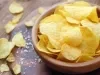Fotografia de um recipiente médio fundo marrom sobre uma mesa de madeira escura. Dentro do recipiente tem chips de batatas, ao lado tem mais algumas juntamente com um pouco de sal grosso sobre a mesa.