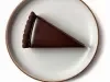 Fotografia vista de cima de uma fatia de torta coberta com chocolate sobre um prato raso claro de vidro.