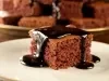 Imagem de um pedaço quadrado de bolo de chocolate sobre um prato claro com calda de chocolate escorrendo.