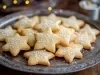 Em cima da mesa, prato com biscoitos crocantes em forma de estrela, decorado confeito branco de bolinhas.