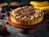 Em cima de uma mesa, banoffee com massa de biscoitos crocante, bananas em rodelas, polvilhado com canela em pó.