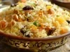 Em cima de uma mesa, tigela redonda coma arroz soltinho, damascos, passas e castanhas, decorado com cheiro-verde picado.