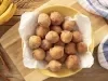 Imagem vista de cima de um bowl amarelo com um guardanapo branco e diversos bolinhos de chuva. Ao lado, bananas e pedaços de canela em pau.
