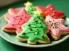 Em cima de uma mesa, prato com biscoitos em formatos de estrela e árvore de natal, decorados com glacê colorido e confeitos coloridas.
