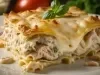 Imagem aproximada de uma fatia de lasanha de frango sobre um prato branco mostrando as camadas e recheio cremoso, gratinado com queijo e decorado com manjericão.