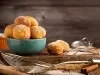 Fotografia de uma tigela de cerâmica teal cheia de bolinhas de massa frita, empilhadas de forma atraente. O cenário rústico inclui uma tábua de madeira polvilhada de açúcar e utensílios de cozinha.