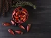 Fotografia vista de uma mesa preta. Sobre a mesa tem um recipiente fundos vermelhos com vários pinhões crus.
