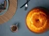 Fotografia de uma mesa elegantemente posta, com um bolo bundt dourado em um prato marrom. Ao lado, há pratos coloridos e um copo de café, com talheres dispostos de forma atraente.