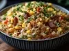 Em cima de uma mesa, tigela com porção de arroz soltinho com pedaços de calabresa picado, milho, pimentão e ervilha, decorado com cheiro-verde picados.