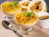 Imagem de duas taças de mousse de maracujá decoradas com sementes de maracujá e folhas de hortelã. Ao lado, duas partes de maracujá ao meio.