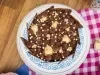 Foto vista de cima de um bolo de chocolate com decoração de lascas marmorizadas, sobre um prato branco e azul em uma bancada de madeira