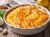 Em cima de uma mesa, refratário com batata gratinada, decorado com cebolinha picada.
