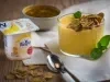 Fotografia em tons de amarelo em uma bancada de madeira, um paninho bege, um potinho com um creme de iogurte de maracujá com gengibre. Ao lado, um potinho de maracujá e uma colher.