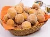 Em cima de uma mesa, cesta de palha com pano laranja com bolinhos de chuva, polvilhado com açúcar de confeiteiro.