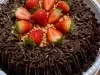 Bolo de chocolate com cobertura cremosa, morangos frescos e crocante granulado, sobre bandeja branca.