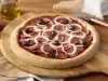 Imagem de uma pizza redonda de calabresa com cebola e azeitonas sobre uma tábua de madeira.