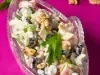 Fotografia de uma salada fresca e colorida em um prato de vidro transparente, composta por melão picado, uvas pretas, nozes e maçãs em um molho cremoso, decorada com salsa fresca, destacando a frescura.