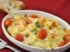 Em cima de uma mesa, refratário com batatas, queijo gratinado e tomates, decorado com folha de salsa.