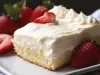 Em cima de uma mesa, prato branco com pedaço de bolo com massa branca, creme branco e morangos cortados ao meio.