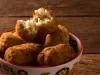 Foto aproximada da receita de Bolinho de Pirarucu, servido em um pote sobre uma bancada de madeira. O Bolinho de cima está aberto pela metade mostrando o interior